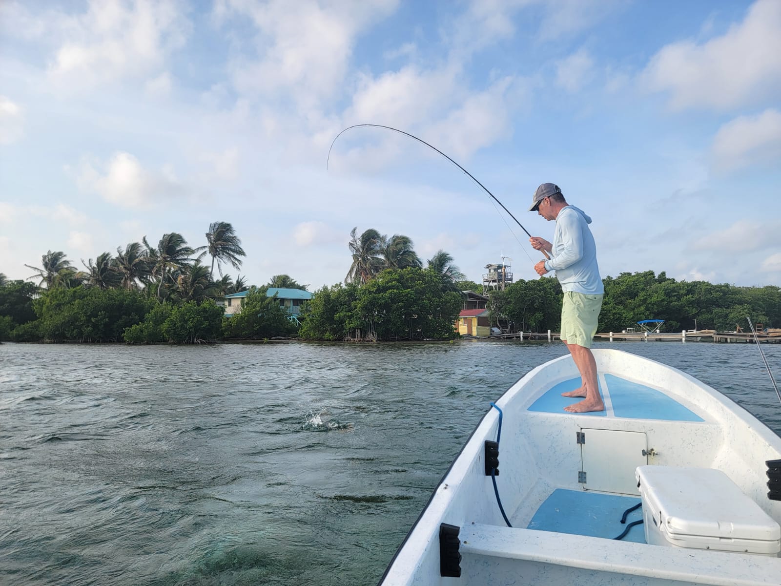 Angler fly fishing in a clear river surrounded by lush green trees and mountains in the background